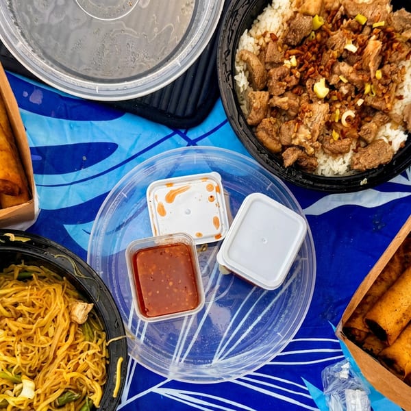 An overhead view of various takeout containers filled with Filipino food, including lumpia, noodles, and rice with meat.