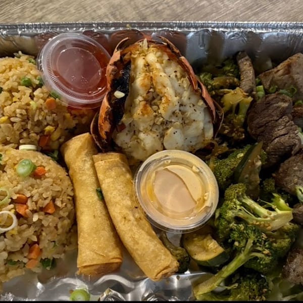 A takeout container with fried rice, lobster tail, egg rolls, steak, and broccoli.