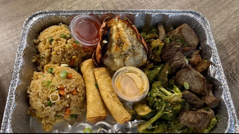 A takeout container with fried rice, lobster tail, egg rolls, steak, and broccoli.