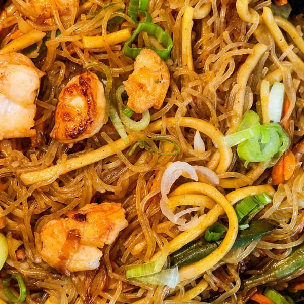Close-up of shrimp and noodles with vegetables, including carrots, green beans, and scallions.