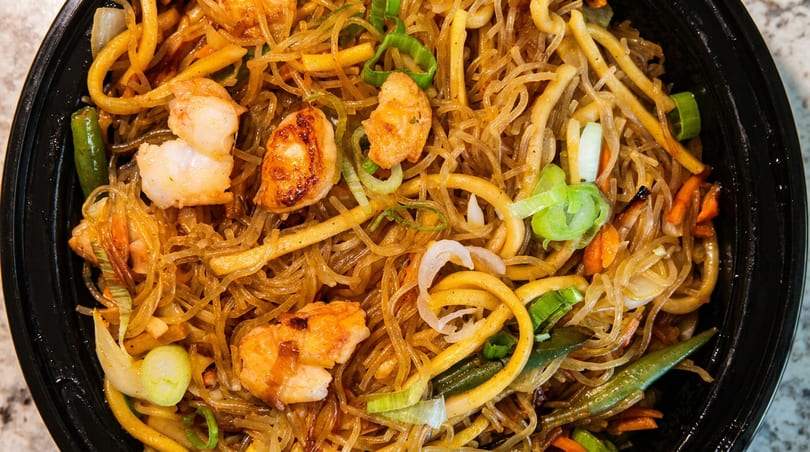 Close-up of shrimp and noodles with vegetables, including carrots, green beans, and scallions.