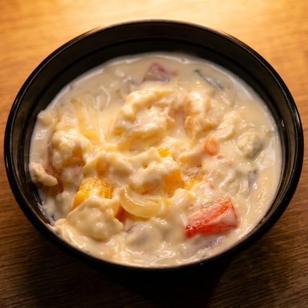 A black bowl filled with creamy fruit salad, featuring peaches, pineapple, and strawberries.