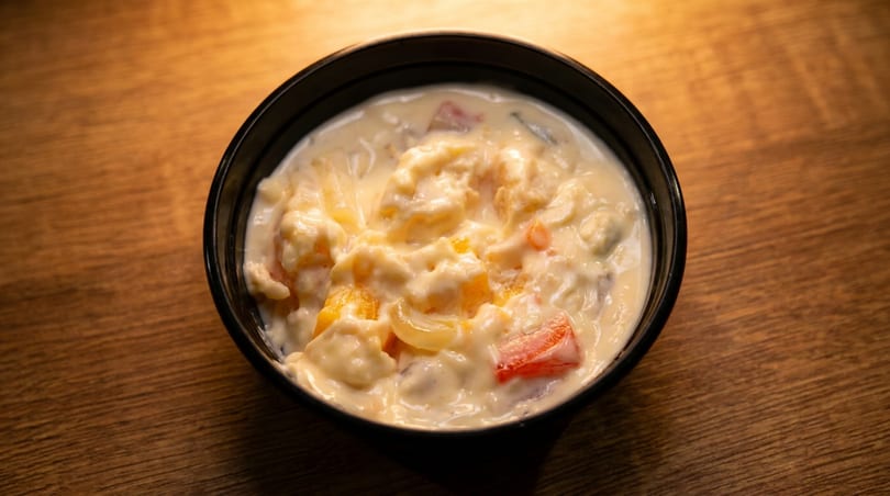 A black bowl filled with creamy fruit salad, featuring peaches, pineapple, and strawberries.